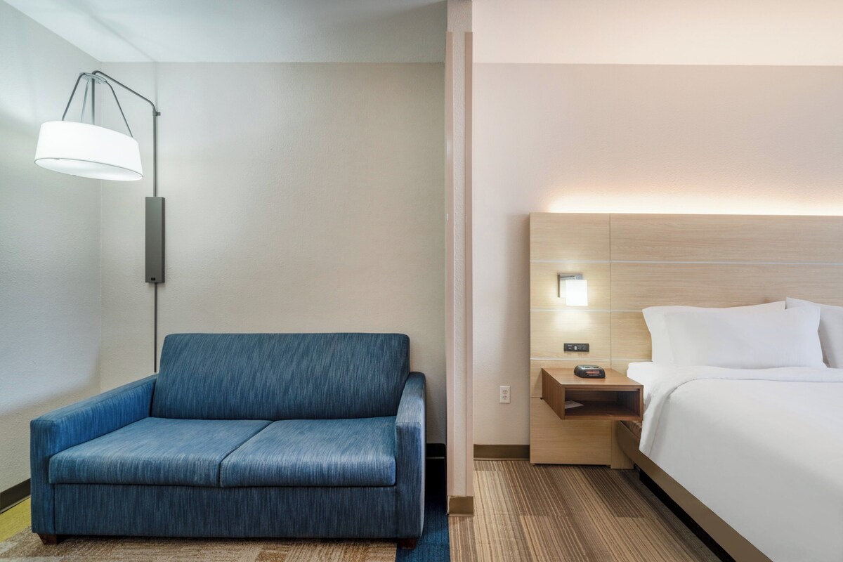 Una camera d'albergo con un divano blu, un letto con lenzuola bianche, un comodino con una lampada e una testiera in legno.