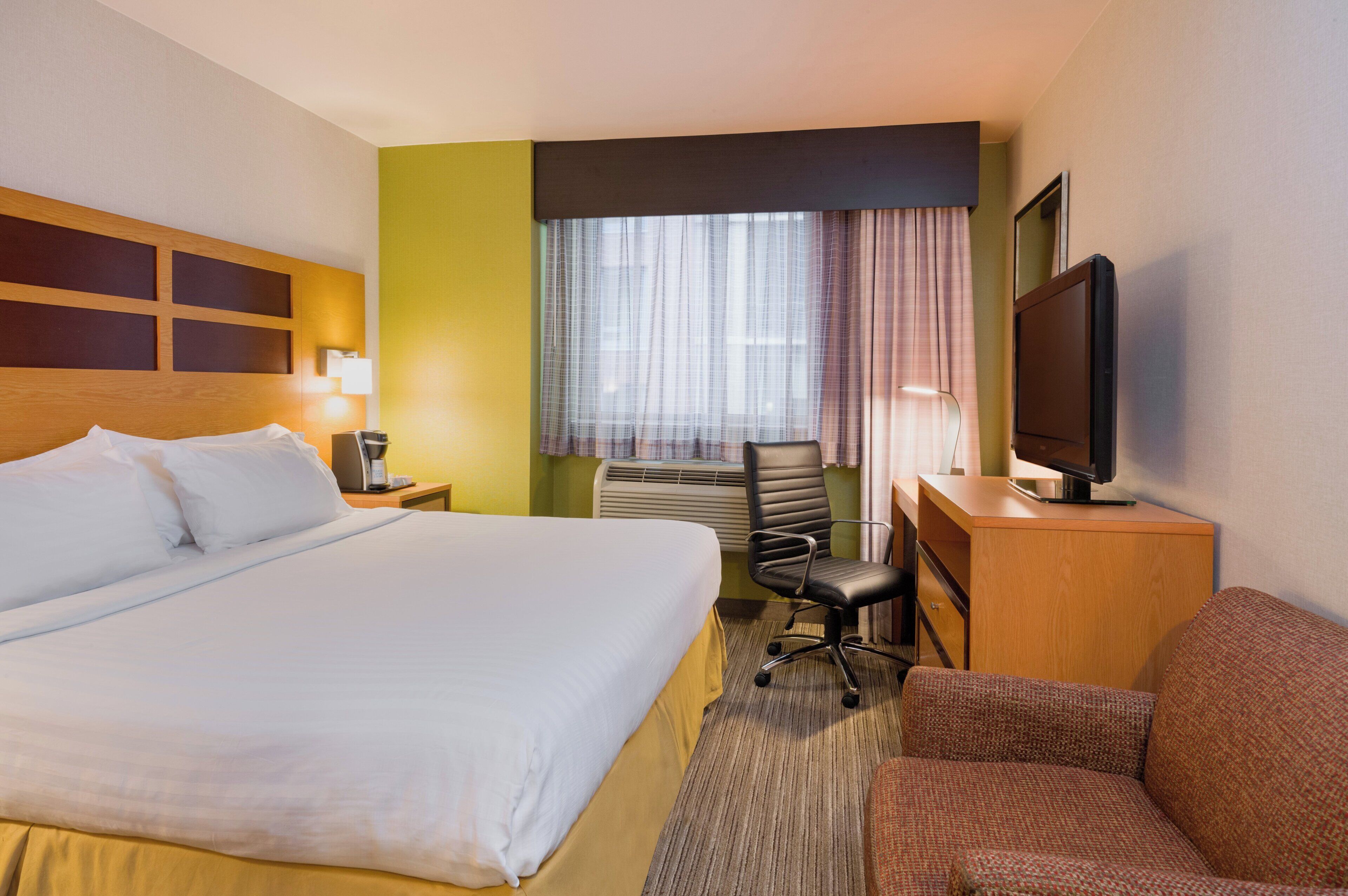 A hotel room with a large bed, a desk with a chair, a television, and a window with curtains.