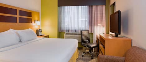 A hotel room with a large bed, a desk with a computer, a chair, a TV, and a window with curtains.