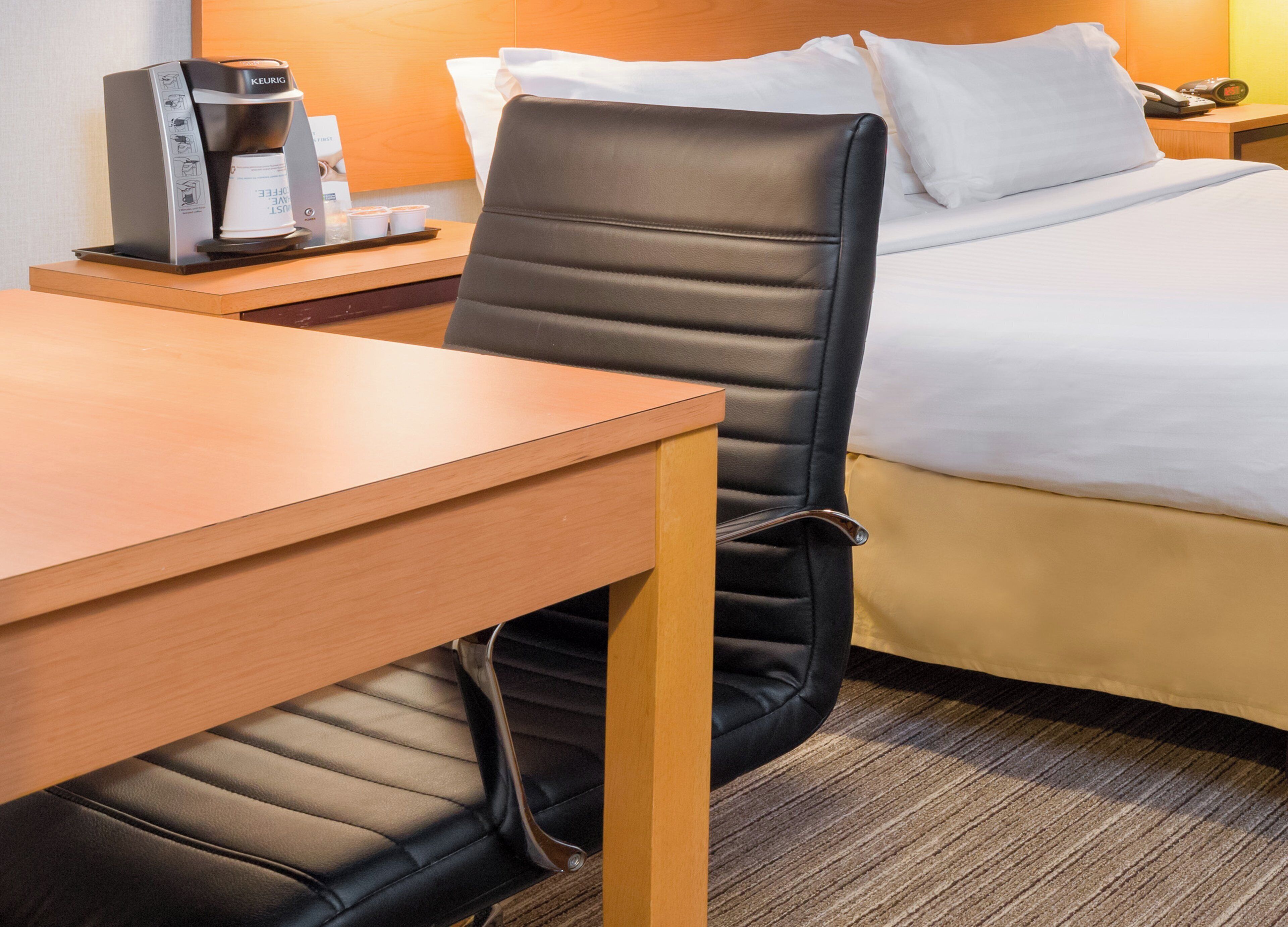 A hotel room with a bed, a desk, a chair, a coffee maker, and a bedside table.