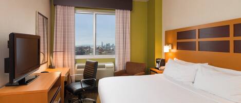 A hotel room with a bed, a desk with a television, a chair, a window with curtains, and a city view.