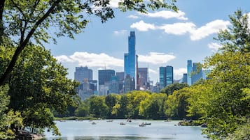 A cityscape with a prominent skyscraper, a river with boats, and dense green trees.