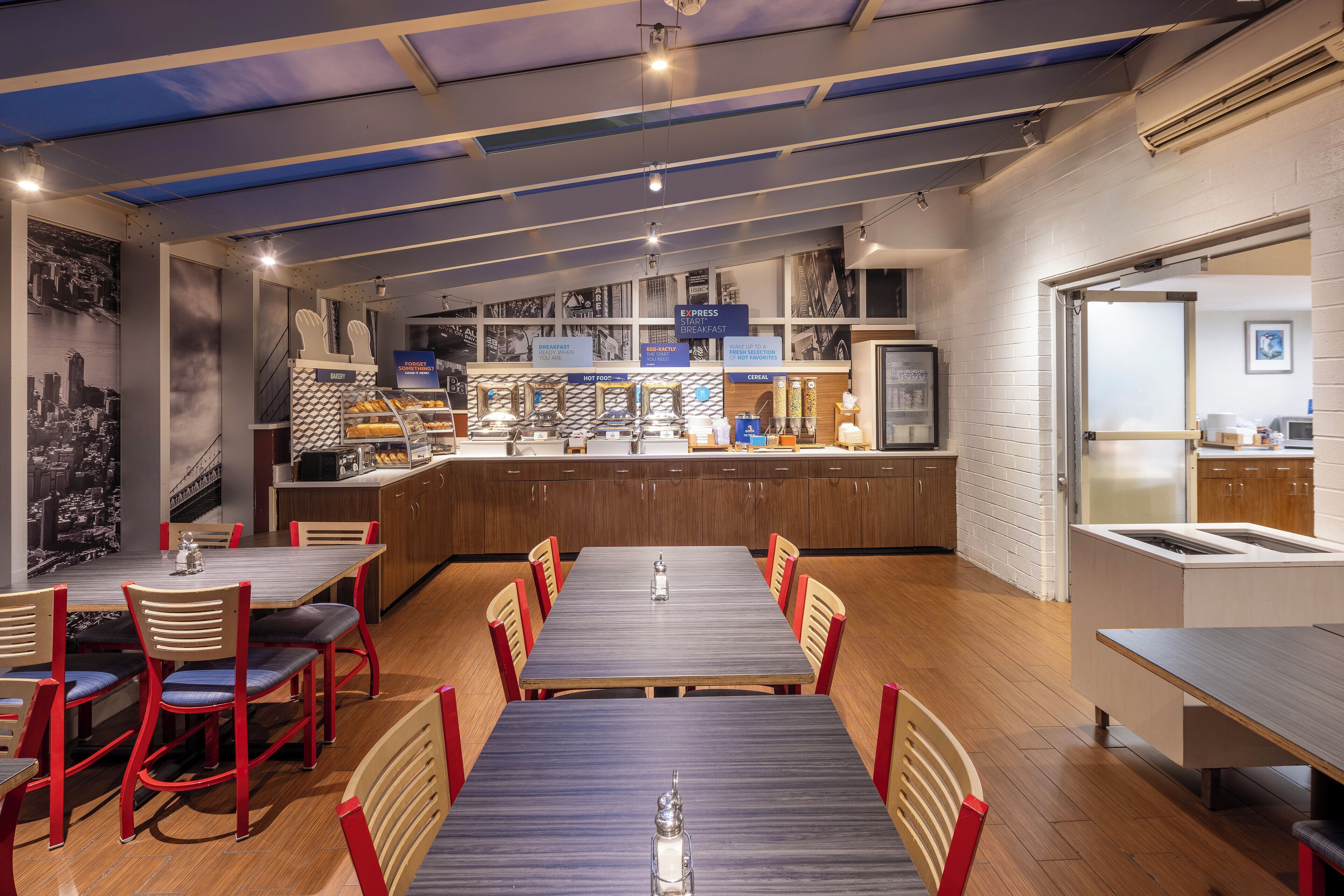 A modern restaurant with a long counter, multiple seating areas, and a cityscape mural on the wall.
