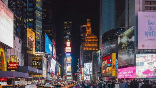 A busy urban street at night with illuminated billboards and skyscrapers.