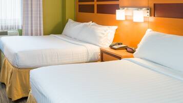 A hotel room with two beds, a nightstand with a phone, and a wall-mounted lamp.