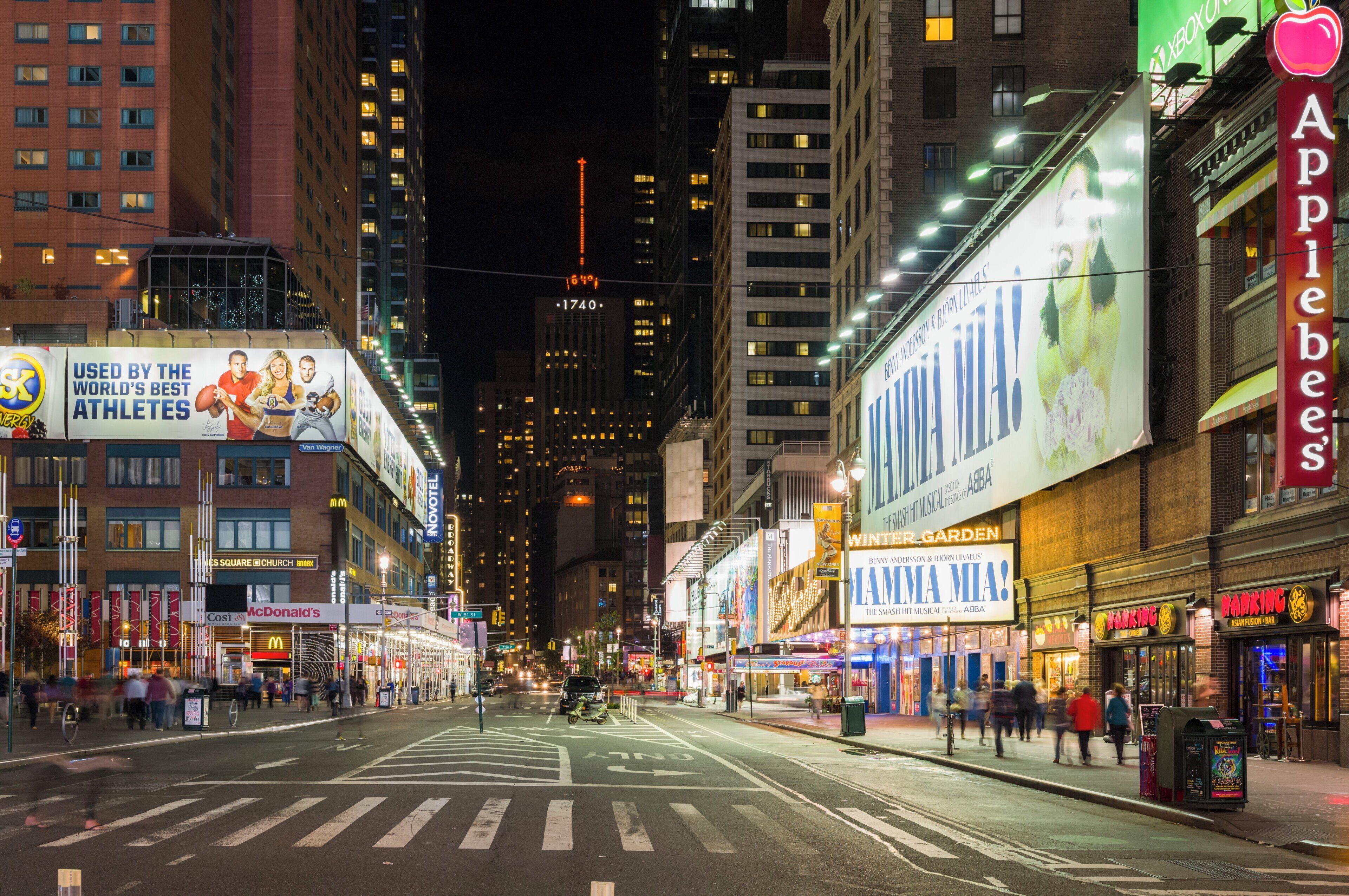 A city street at night with illuminated billboards and storefronts.