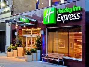 Um Holiday Inn Express com um logotipo verde chamativo, entrada de vidro e plantas em vasos na parte externa.