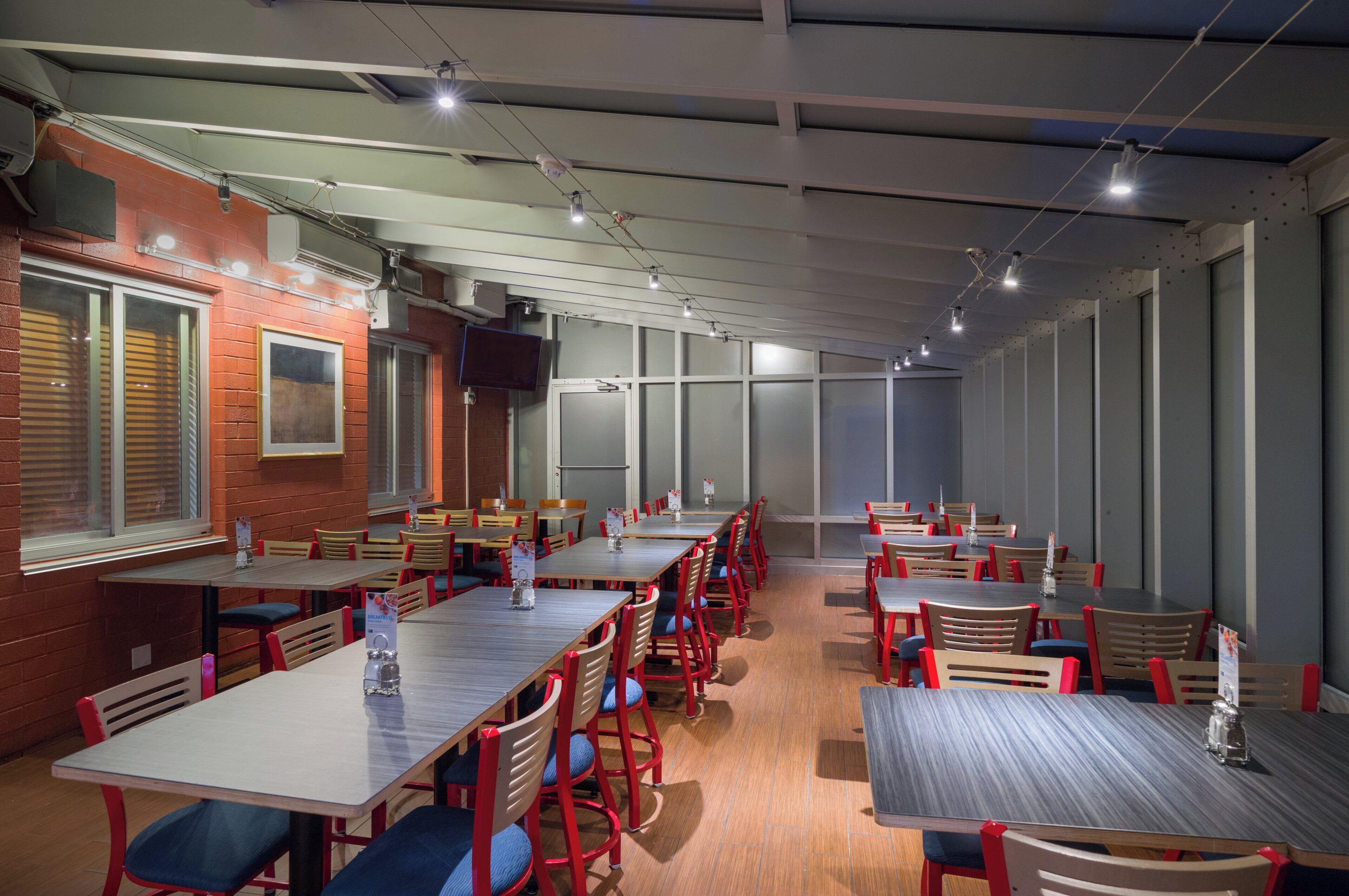 A dining area with multiple tables and chairs, a brick wall, and a large window.