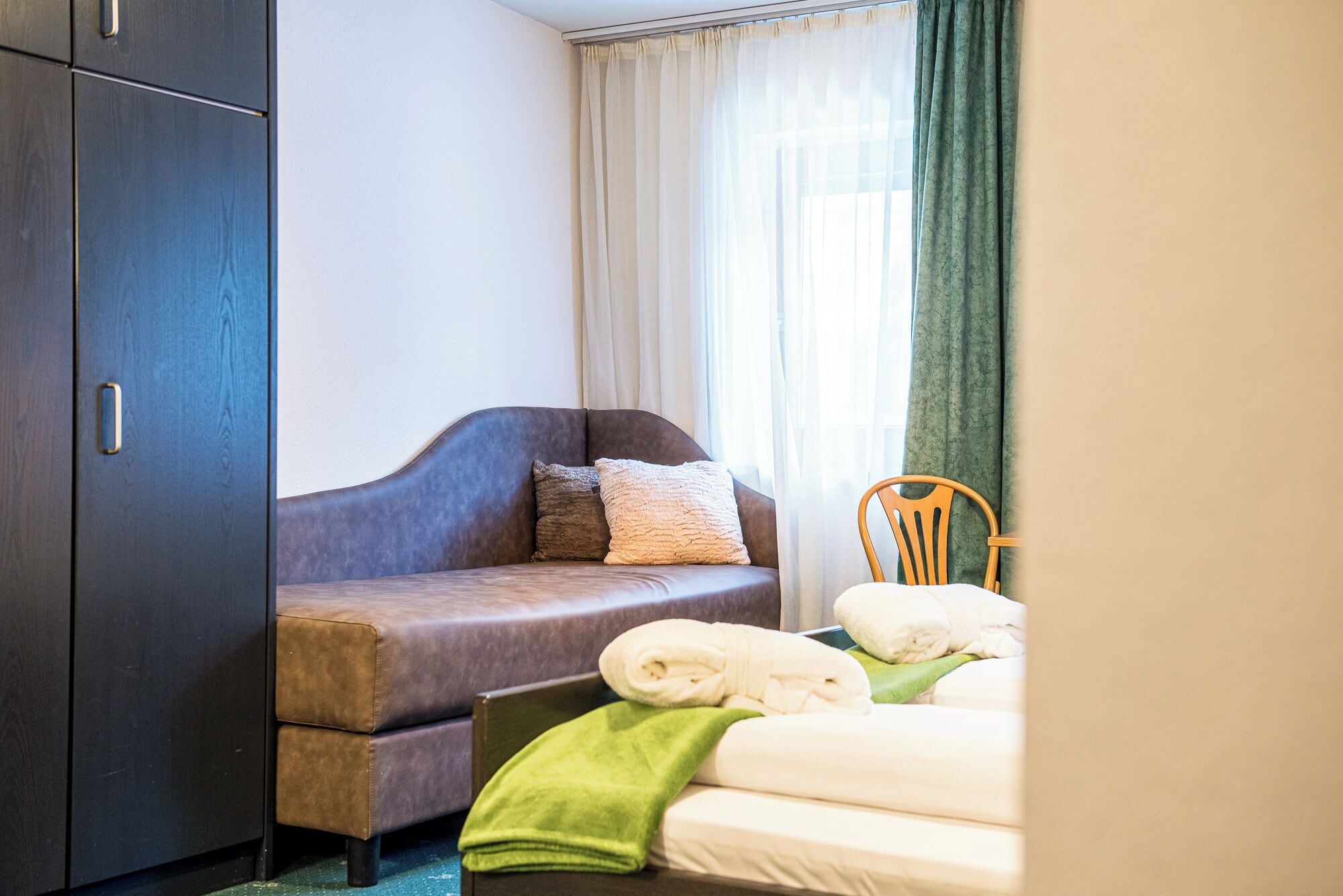 Ein Hotelzimmer mit einer Couch, einem Sessel, einem Bett und einem Kleiderschrank.