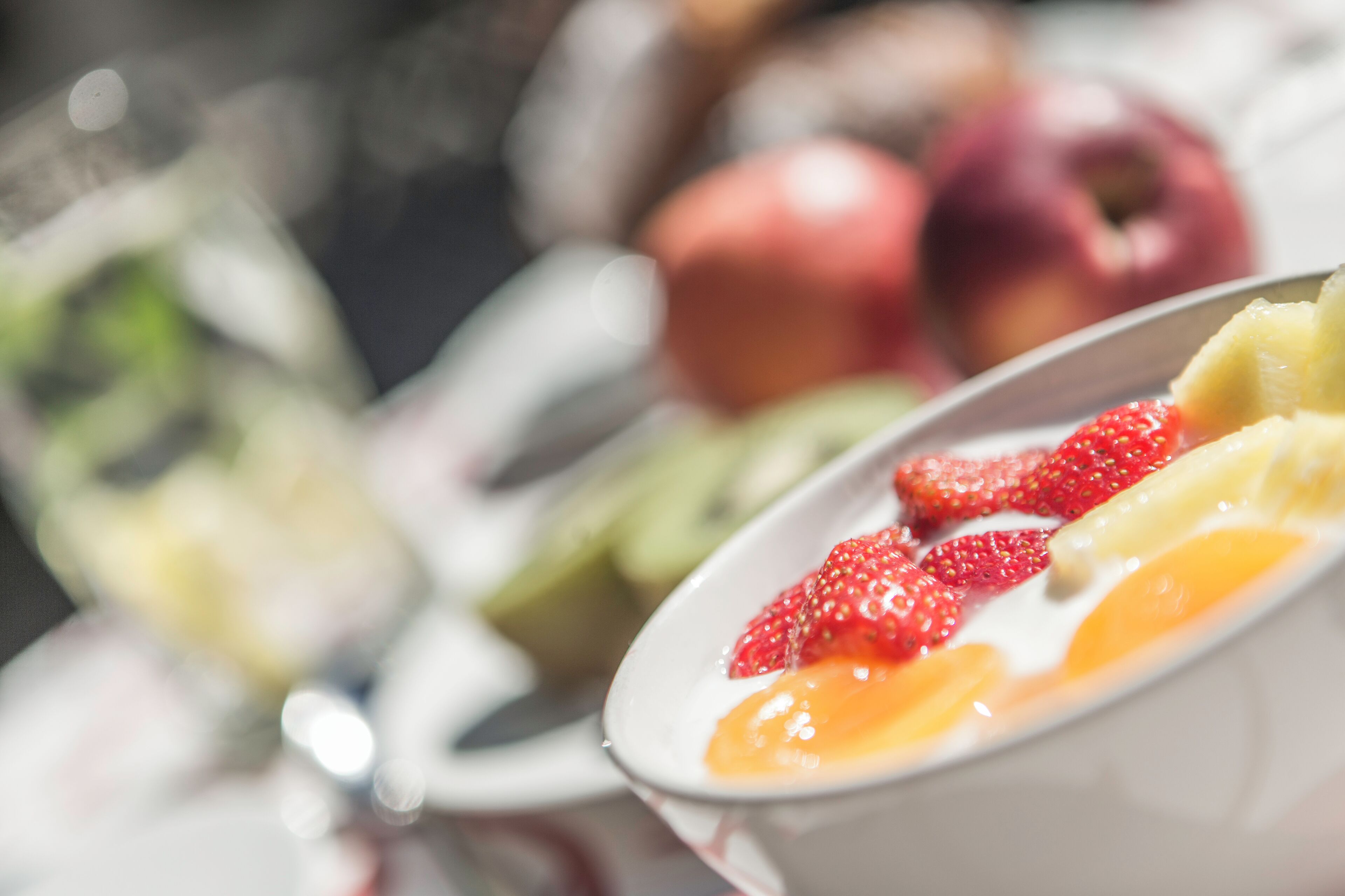 Un tazón de ensalada de frutas con fresas y kiwi, y un vaso de agua al fondo.