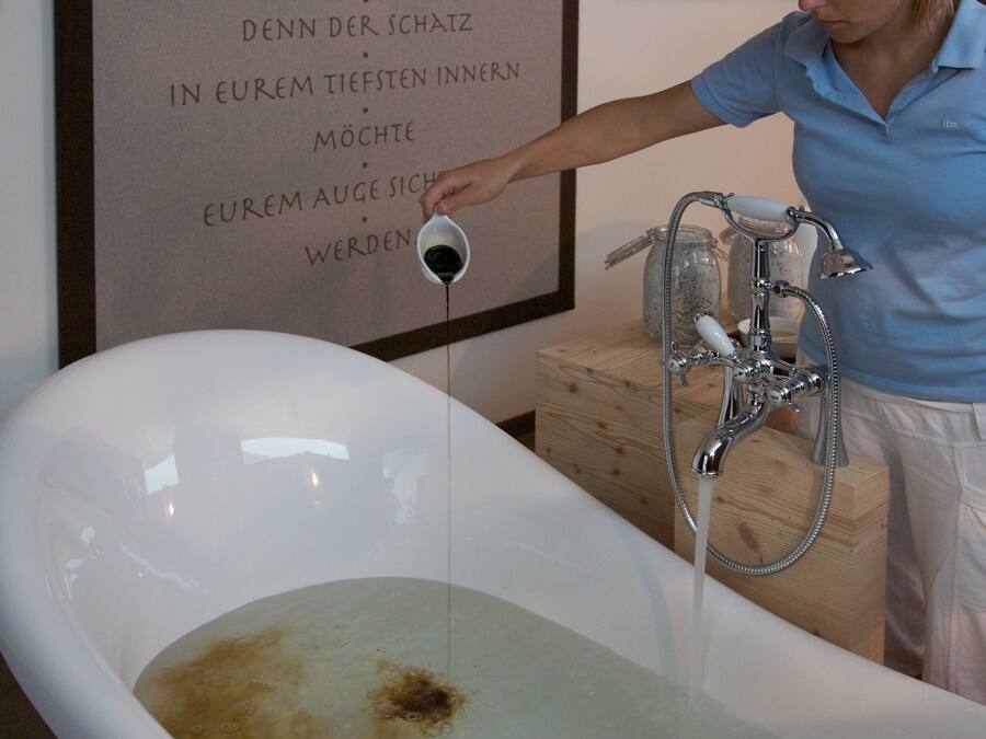 A bathtub with running water, a wooden cabinet, and a wall with text in German.