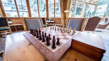 A wooden chessboard set on a table in a room with large windows and wooden furniture.