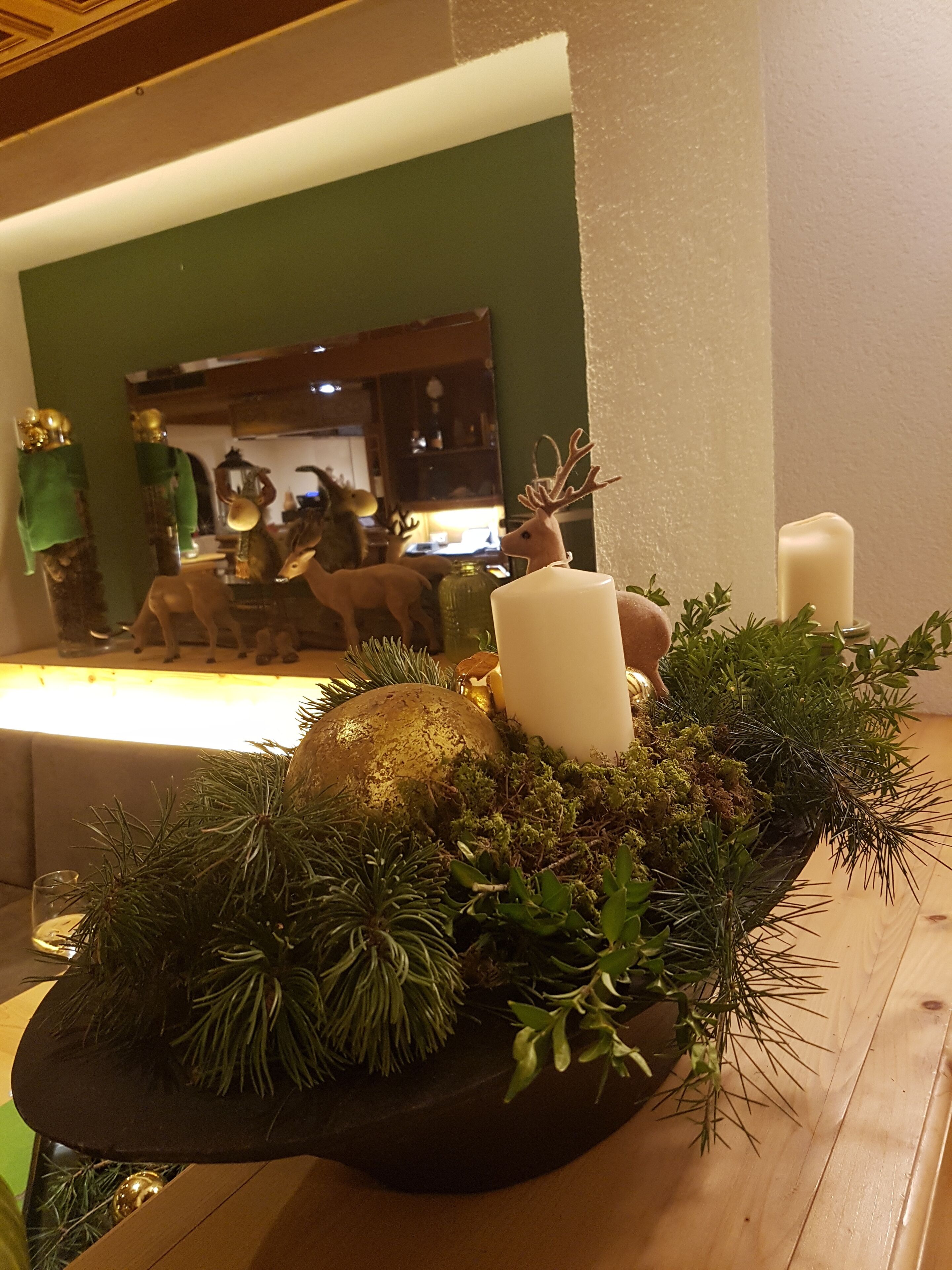 A table with a decorative centerpiece featuring a candle, a golden ornament, and green foliage.
