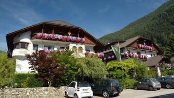 Ein traditionelles Chalet mit Balkonen, die mit Blumen geschmückt sind, einer Steinsäule und parkenden Autos davor.
