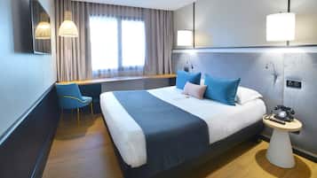 Habitación de hotel moderna con una cama grande, un escritorio, una silla y una mesita de noche con teléfono.