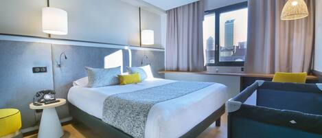 A modern hotel room with a large bed, bedside tables, a desk, and a view of the city.