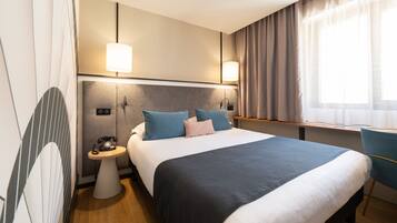 Una habitación de hotel con una cama grande, lámparas de noche, una mesita con un teléfono y una silla.