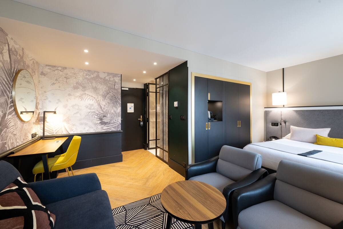 A modern hotel room with a bed, seating area, and a dining table.