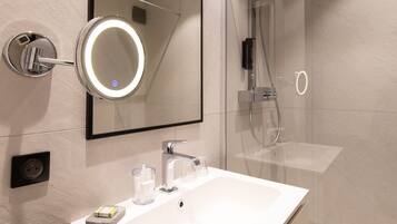 A modern bathroom with a white sink, a mirror with a circular light, a glass shower enclosure, and a toilet.