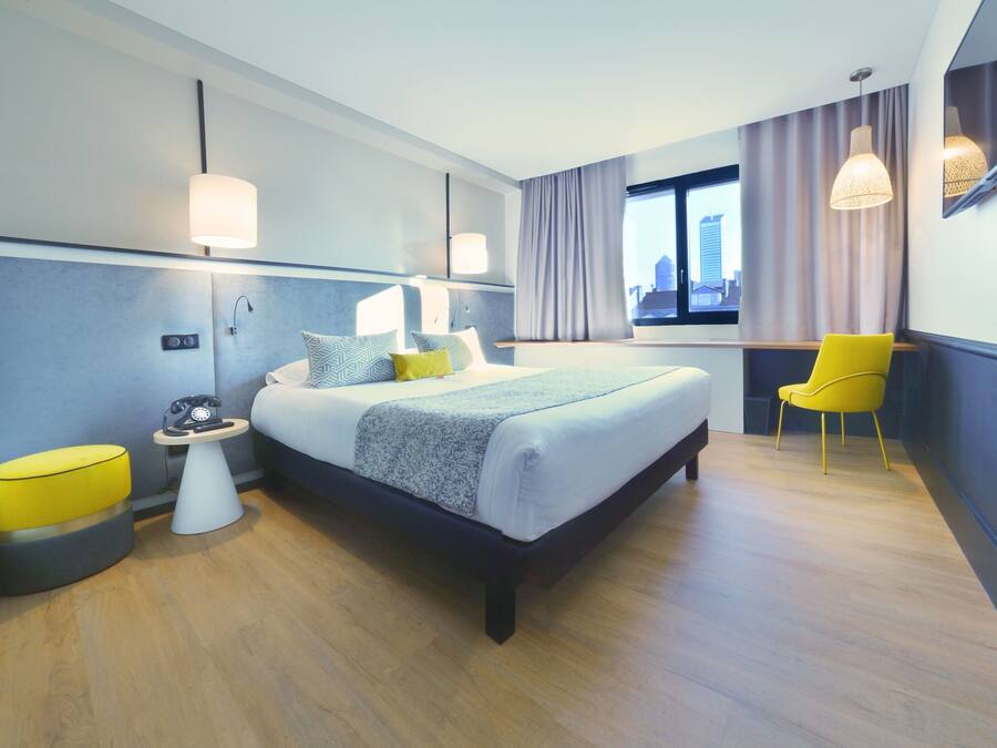 A modern hotel room with a large bed, bedside tables, a chair, and a city view through the window.