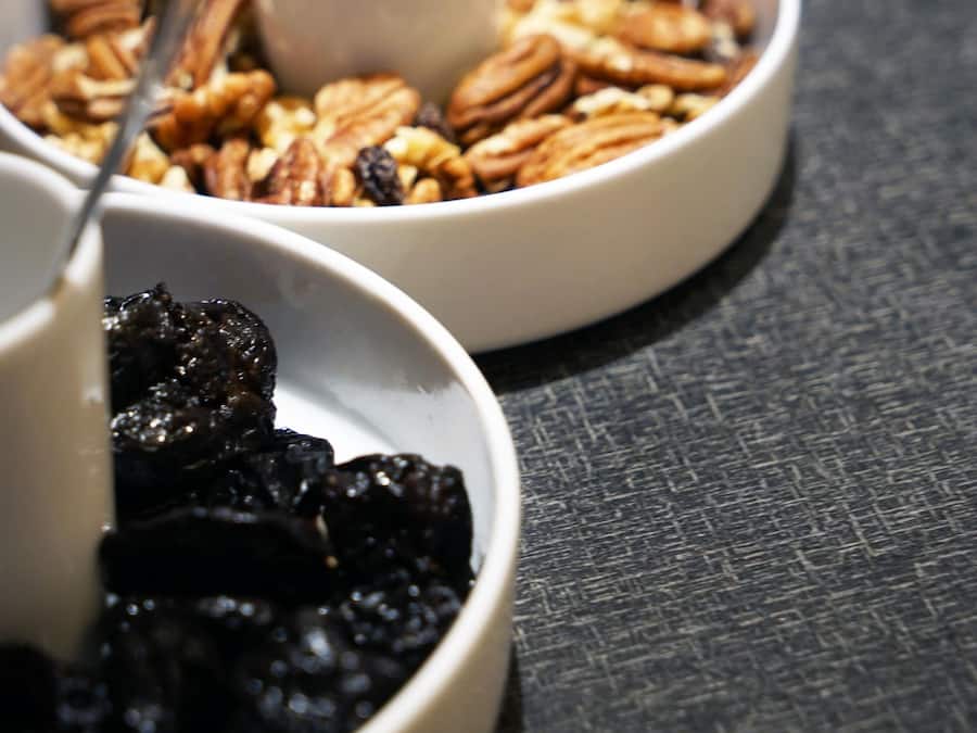 A table with bowls of nuts and dried fruits, a spoon, and a white mug.