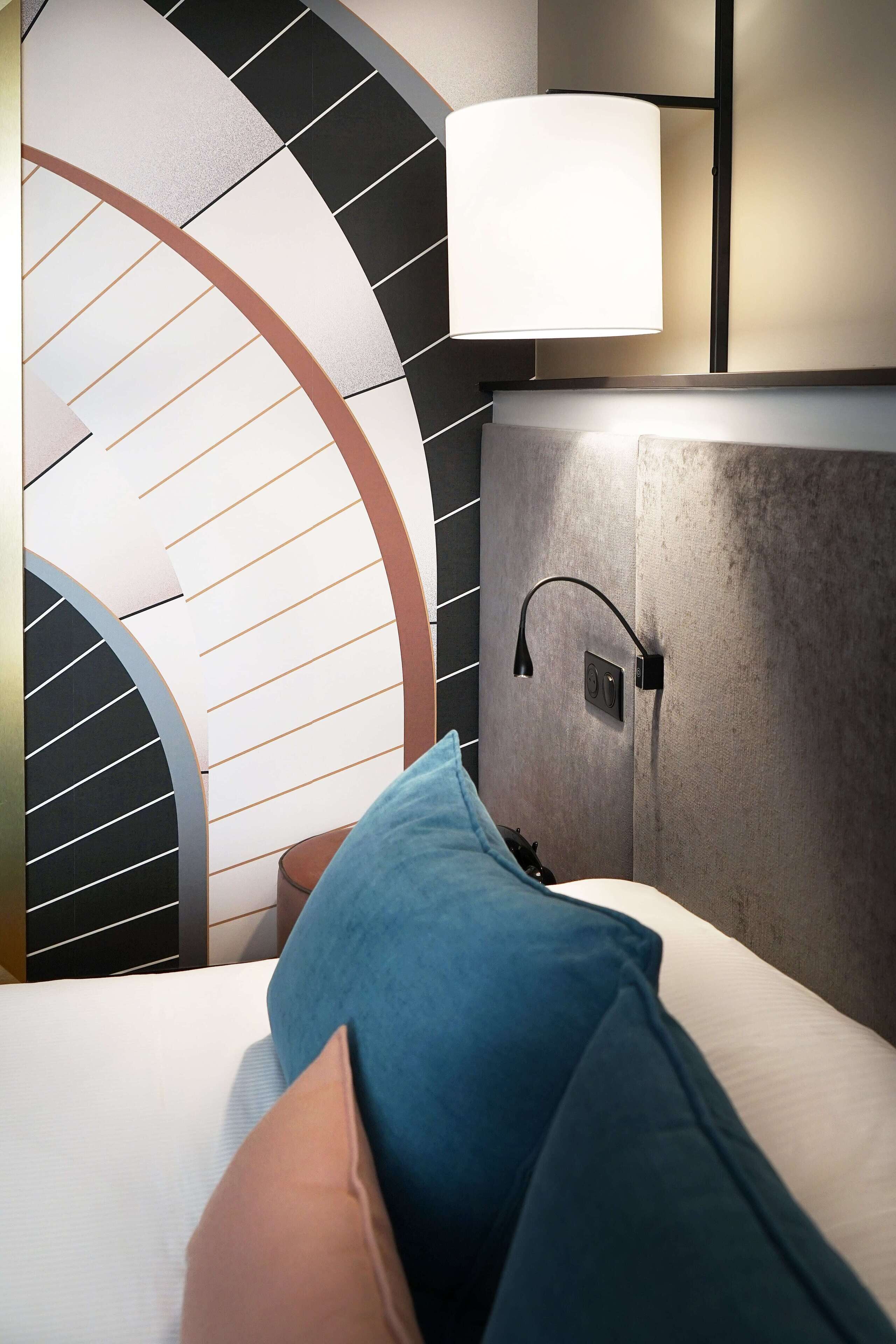 Ein modernes Hotelzimmer mit einer gebogenen Treppe, einem Bett mit blau und beige gestreiften Kissen und einer Wandlampe.
