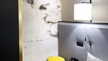Habitación de hotel con un cuadro abstracto grande en la pared, una mesita de noche con una lámpara, un teléfono y un cojín estampado.