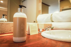 Un baño con encimera de madera, una botella de jabón líquido, un lavamanos blanco y una toalla blanca.