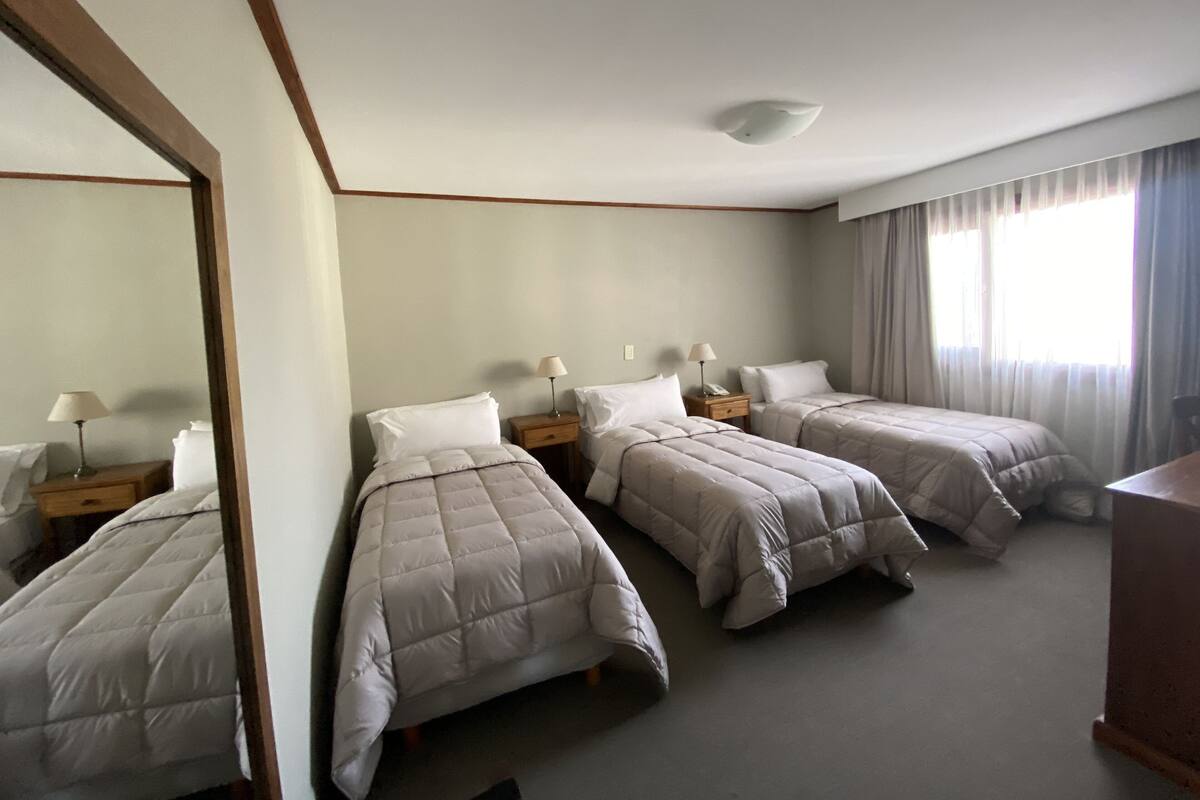 Een hotelkamer met twee enkele bedden, een grote spiegel, een nachtkastje met een lamp en een raam met gordijnen.