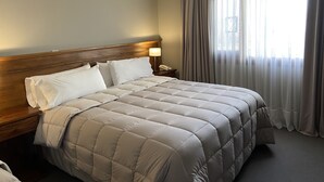 A hotel room with a large bed, wooden headboard, a bedside table with a lamp, and a window with sheer curtains. - Sent Calafate (El Calafate)