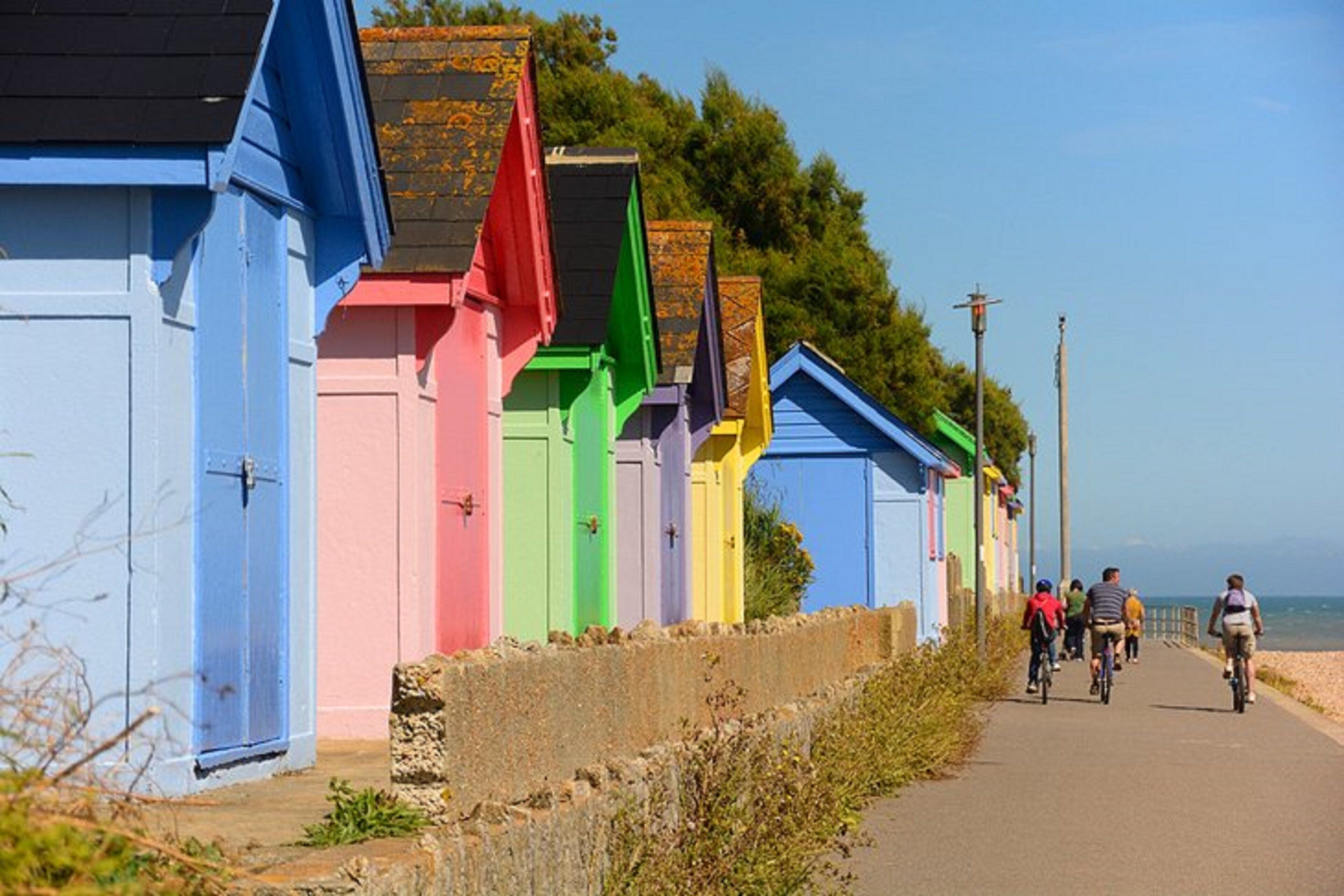 Una hilera de coloridas cabañas frente al mar, con un camino que lleva a la playa.