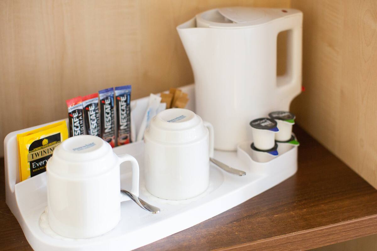 A coffee station with a coffee maker, two cups, a spoon, and coffee pods.