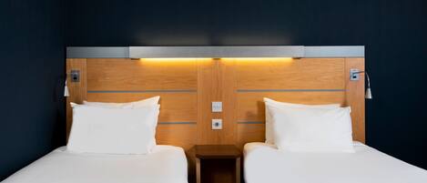 A hotel room with two single beds, wooden headboard, bedside lamps, and a small wooden nightstand.