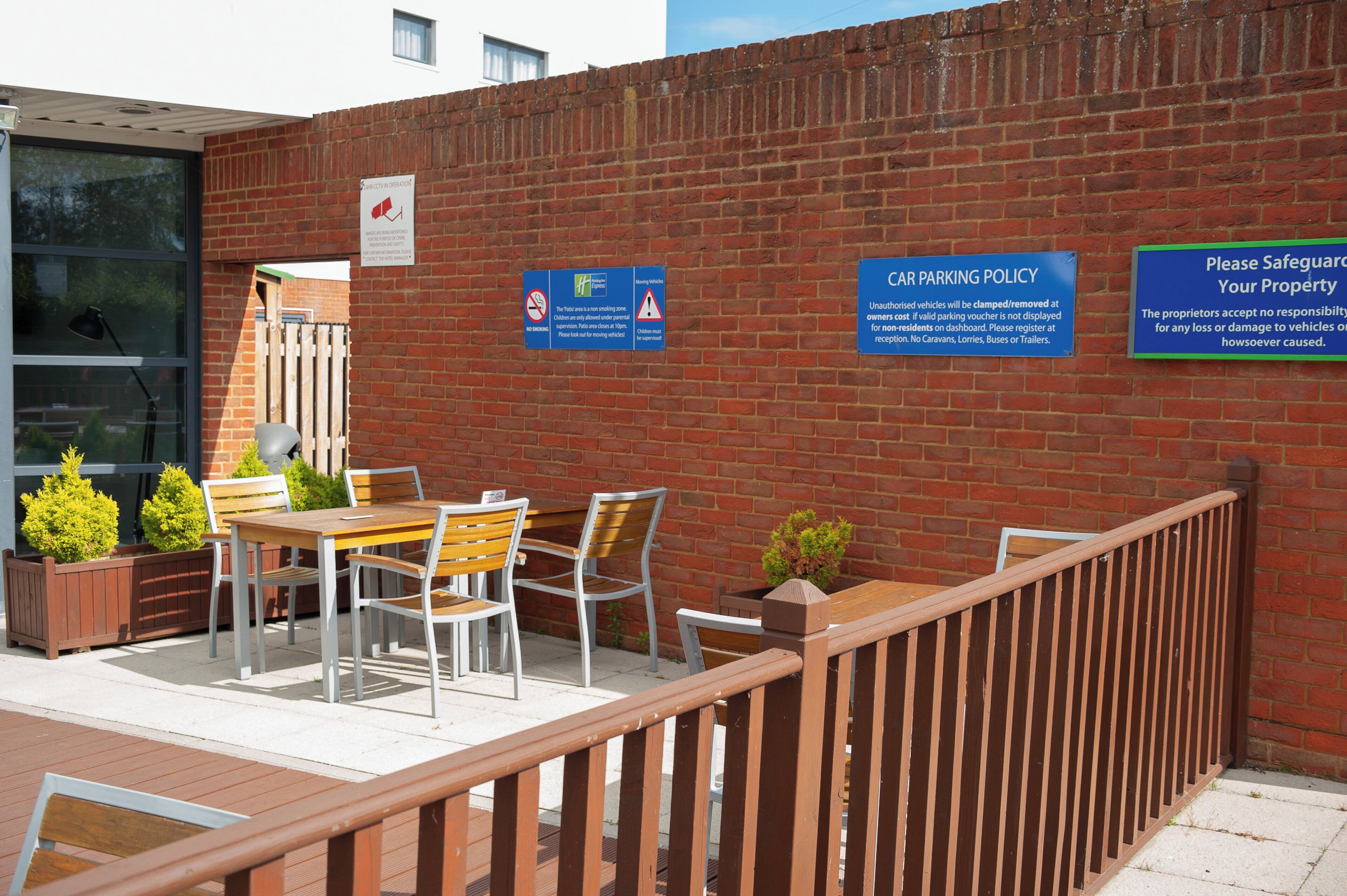 An outdoor seating area with a brick wall, a table with chairs, and a sign indicating a car parking policy.