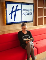 Una persona sentada en un banco rojo en el vestíbulo de un Holiday Inn Express, sosteniendo un libro.