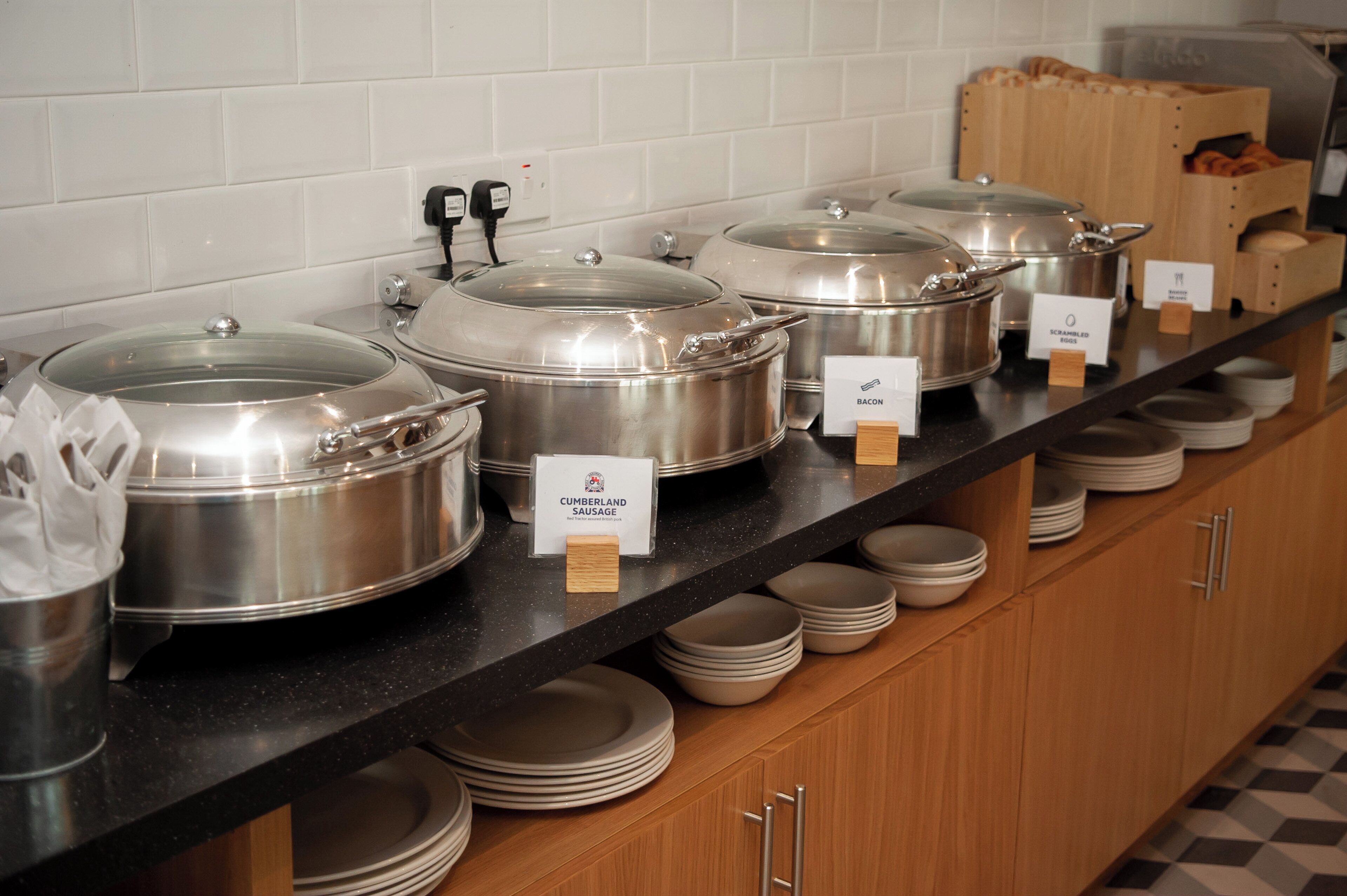 A buffet setup with covered food containers labeled with food types like Cumberland Sausage and Bacon.
