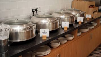 A buffet setup with covered food containers labeled with food types like Cumberland Sausage and Bacon.