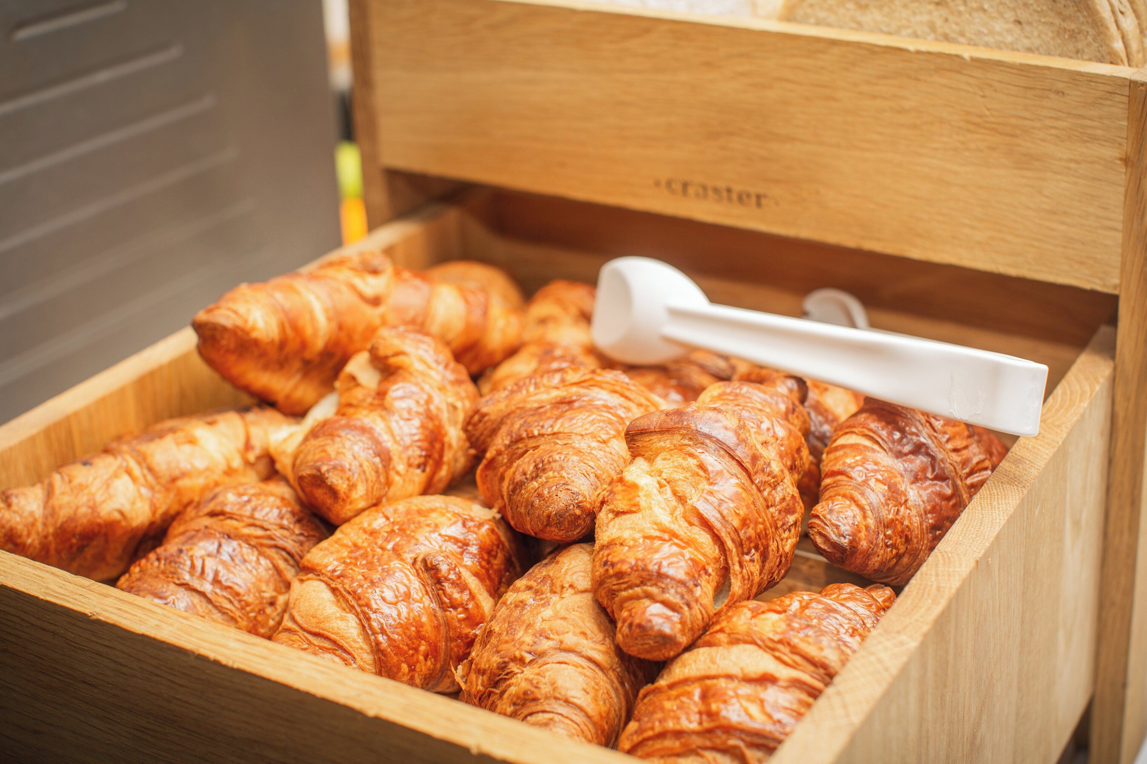 A wooden box filled with croissants and a white measuring spoon.