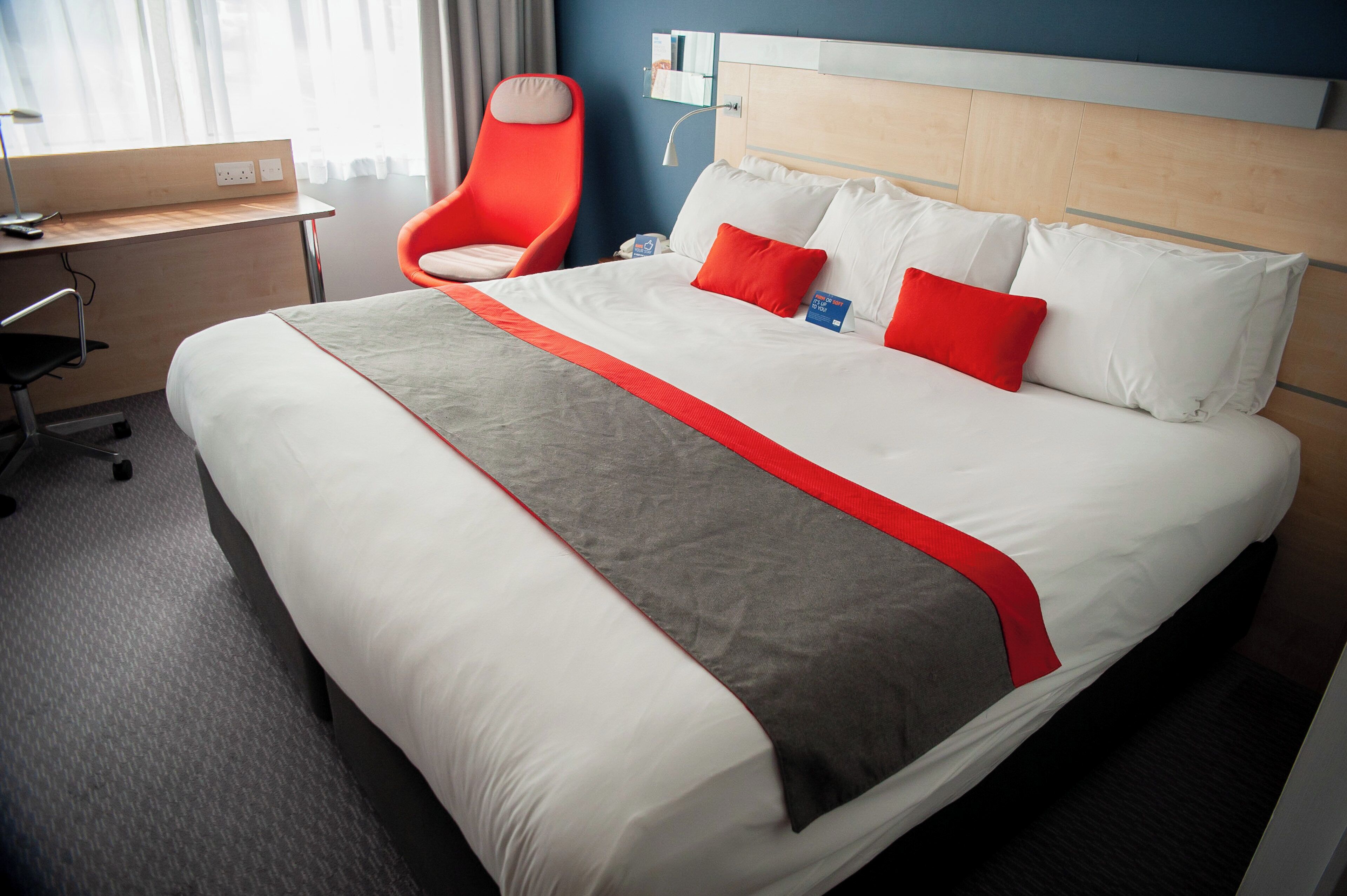 Een hotelkamer met een groot bed, een bureau, een stoel en een nachtkastje.