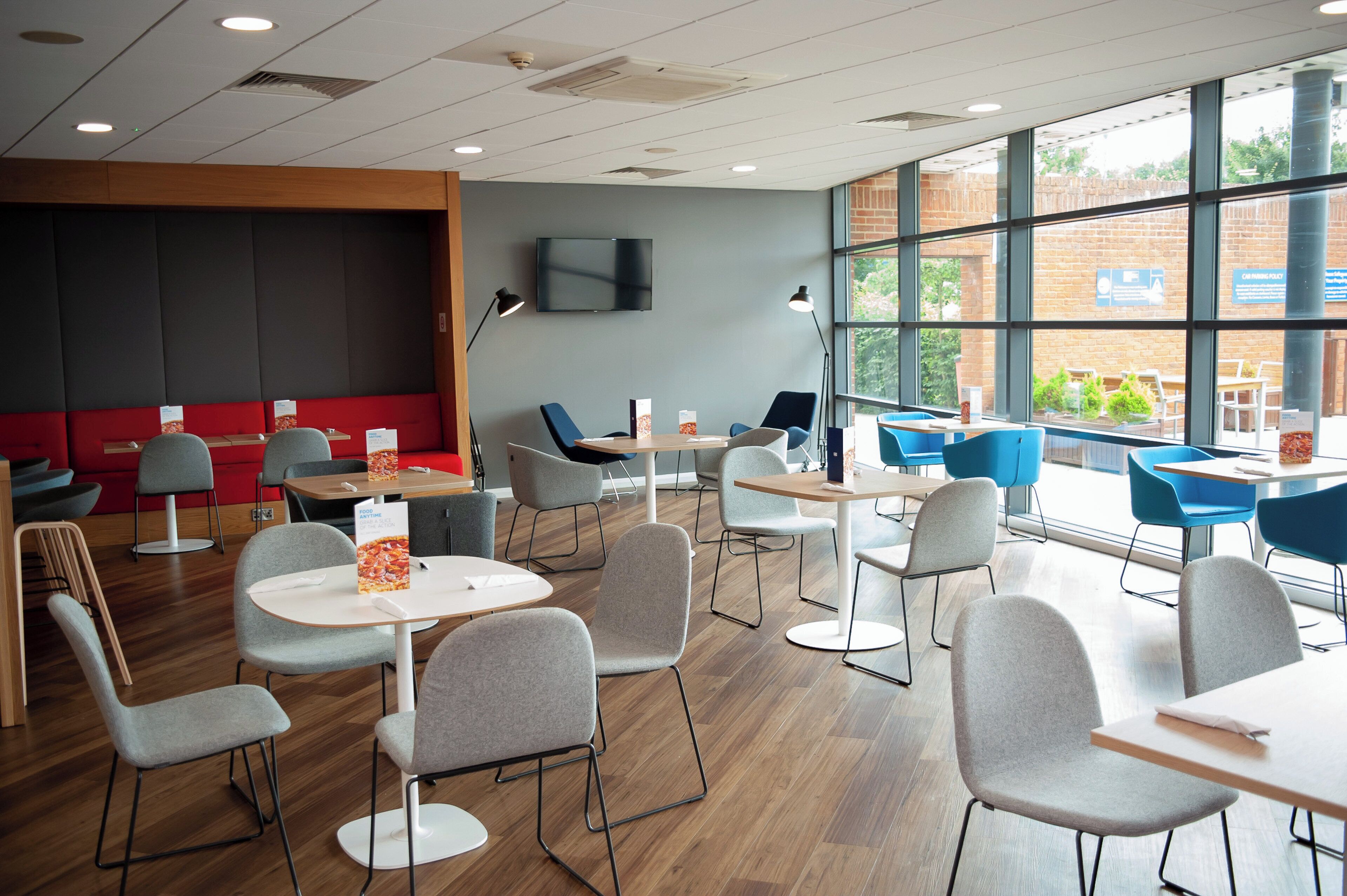 A modern indoor space with multiple seating areas, including tables and chairs, and a large window providing a view of the outdoors.