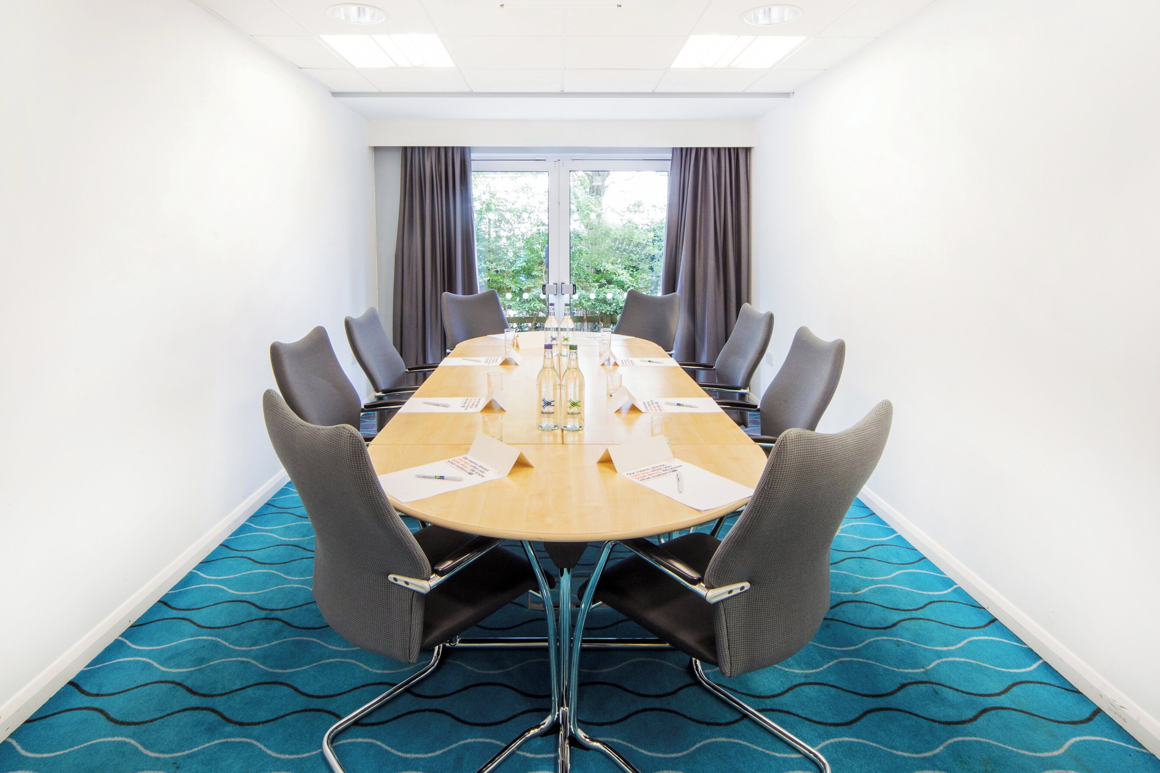 Uma sala de conferências com uma mesa comprida, cadeiras e vista para árvores pelas janelas.