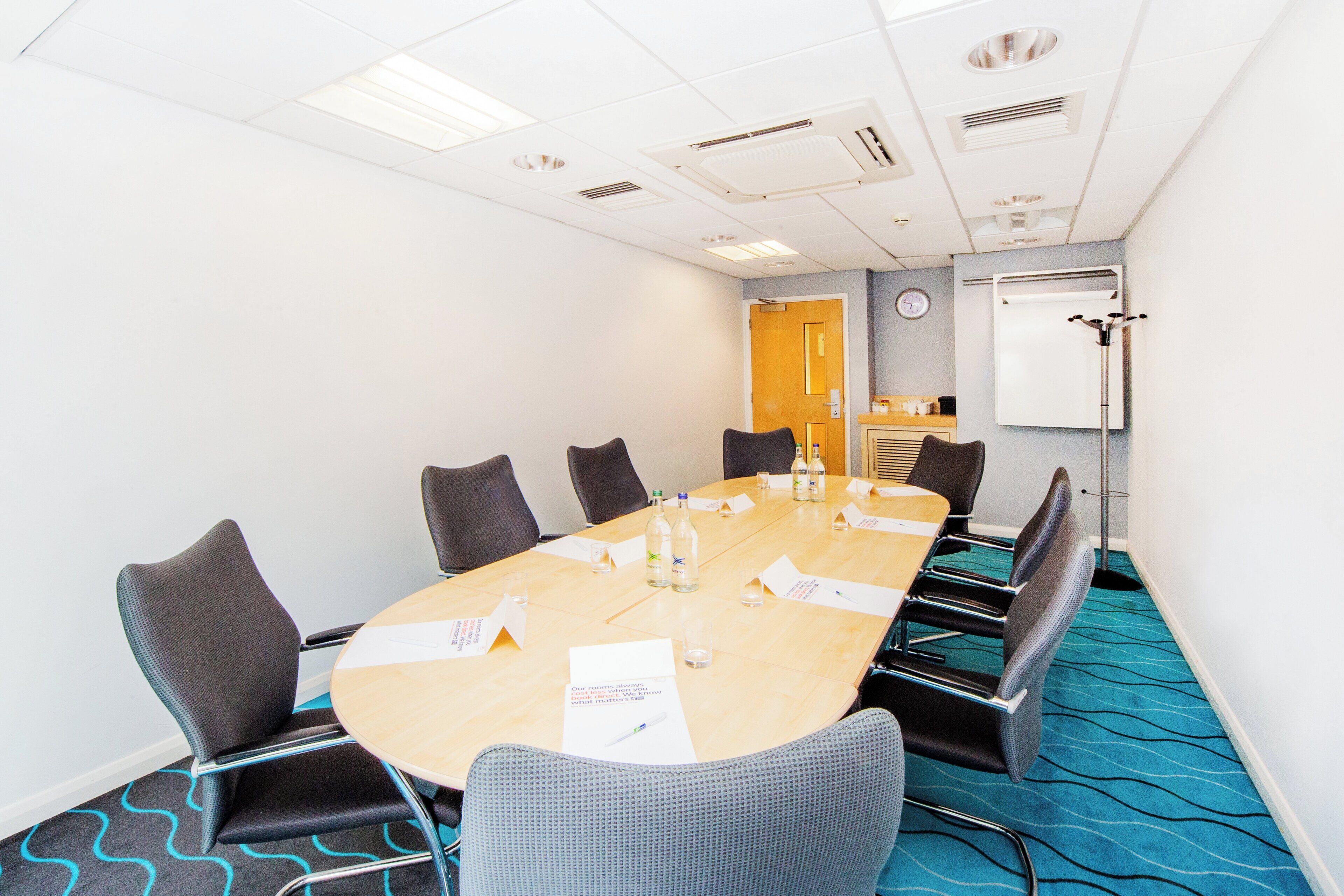 A conference room with a long table, chairs, a clock, and a whiteboard.