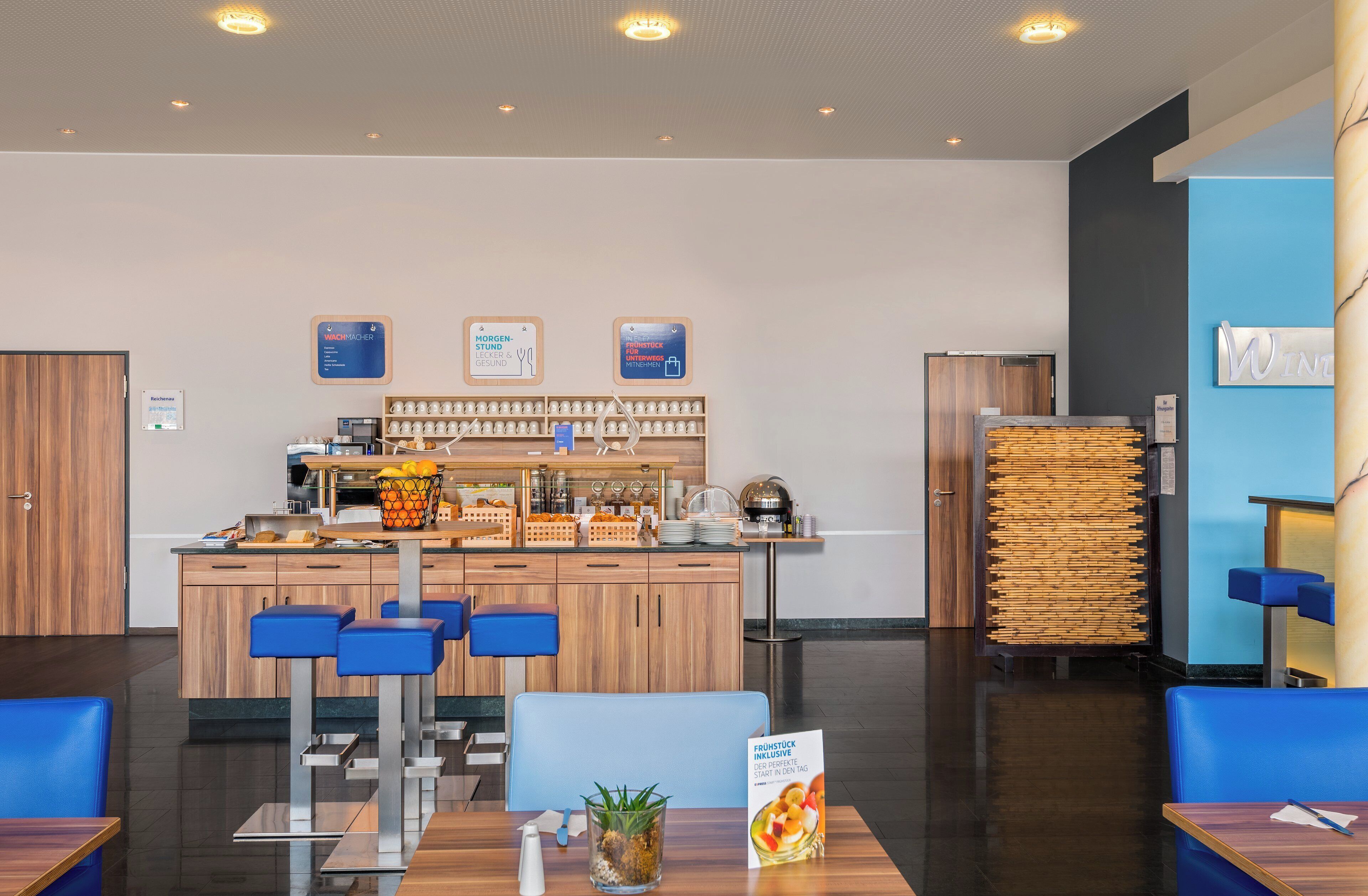 Un moderno vestíbulo de hotel con barra de desayuno, zona de estar y mostrador de recepción.