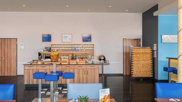 Un moderno vestíbulo de hotel con barra de desayuno, zona de estar y mostrador de recepción.
