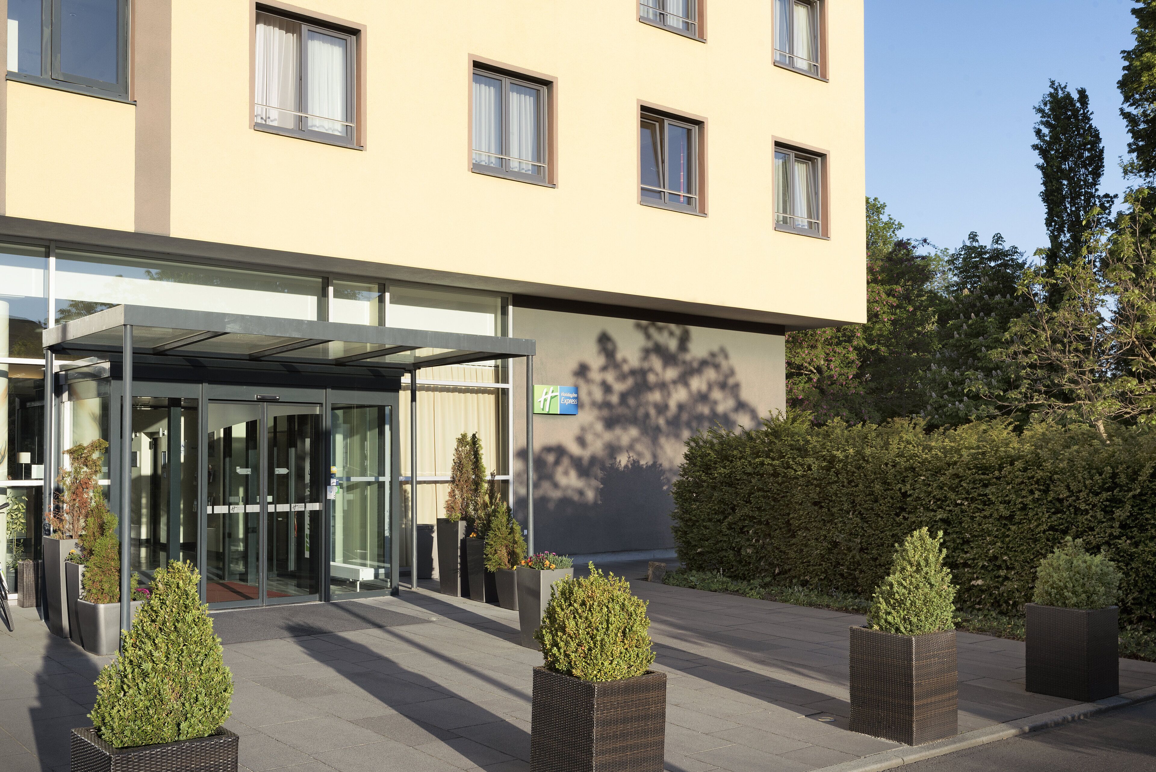 A hotel entrance with a glass door, a covered walkway, and potted plants.
