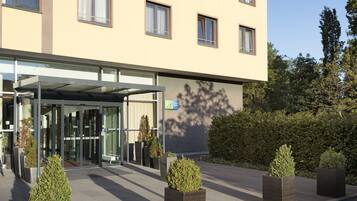 A hotel entrance with a glass door, a covered walkway, and potted plants.