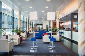 A modern hotel lobby with seating areas, a reception desk, and large windows.