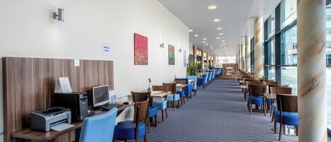 Un vestíbulo de hotel con un mostrador de recepción alargado, varias zonas de estar y grandes ventanales.
