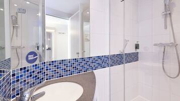 Un baño moderno con cabina de ducha de vidrio, un lavamanos blanco sobre encimera de mármol y un salpicadero con azulejos azules.
