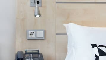 Habitación de hotel con teléfono en la mesita de noche, toma de corriente e iluminación empotrada en la pared.